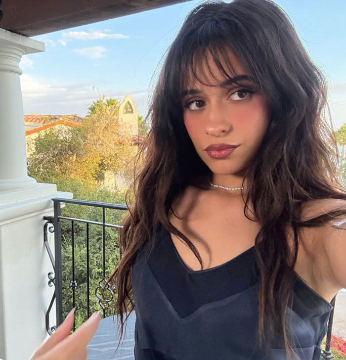 Young woman with long dark hair and a black dress posing outdoors with nature background at a star-studded wedding event