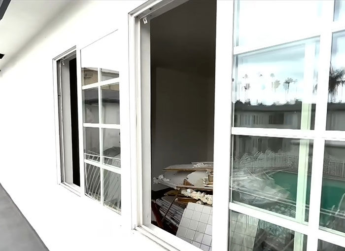 Exterior view of a white home with broken windows and debris inside, related to American nightmare online marriage case.