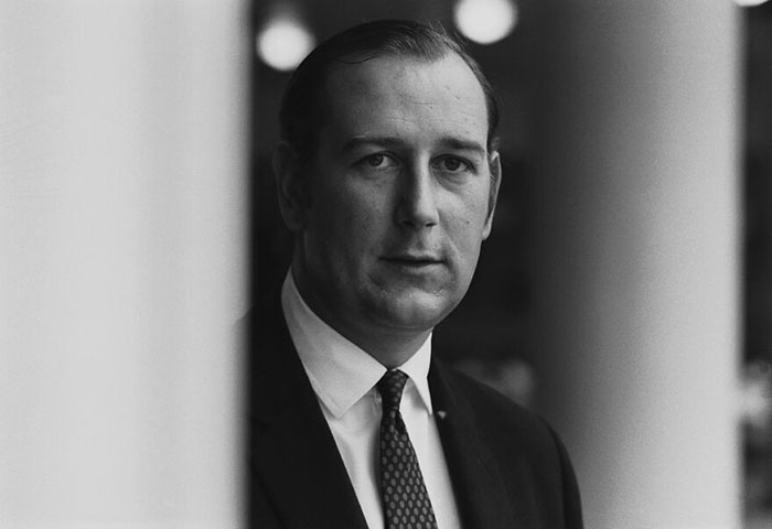 Black and white portrait of a serious male celebrity in a suit, related to male celebrities slain by women topic.
