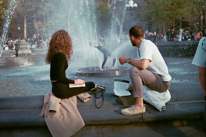 Two people sitting by a fountain in a crowded urban park, captured in a striking street photo with cinematic style.