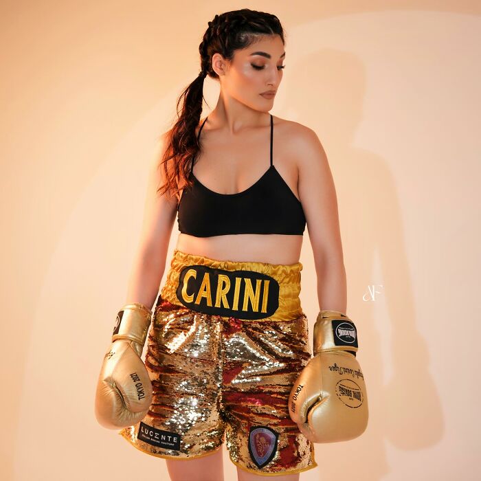 Female boxer wearing golden boxing gloves and sequin shorts, standing confident while reflecting on harassment that affected her career.