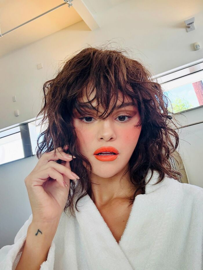 Selena Gomez with curly hair and bright lipstick, posing indoors in a white robe, related to wedding snub controversy. Selena Gomez with curly hair and bright lipstick, posing indoors in a white robe, related to wedding snub controversy.