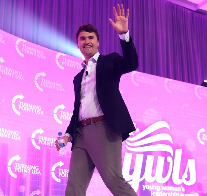 Man waving on stage at Turning Point USA event, related to woman discovering hidden hate message on Starbucks cup.