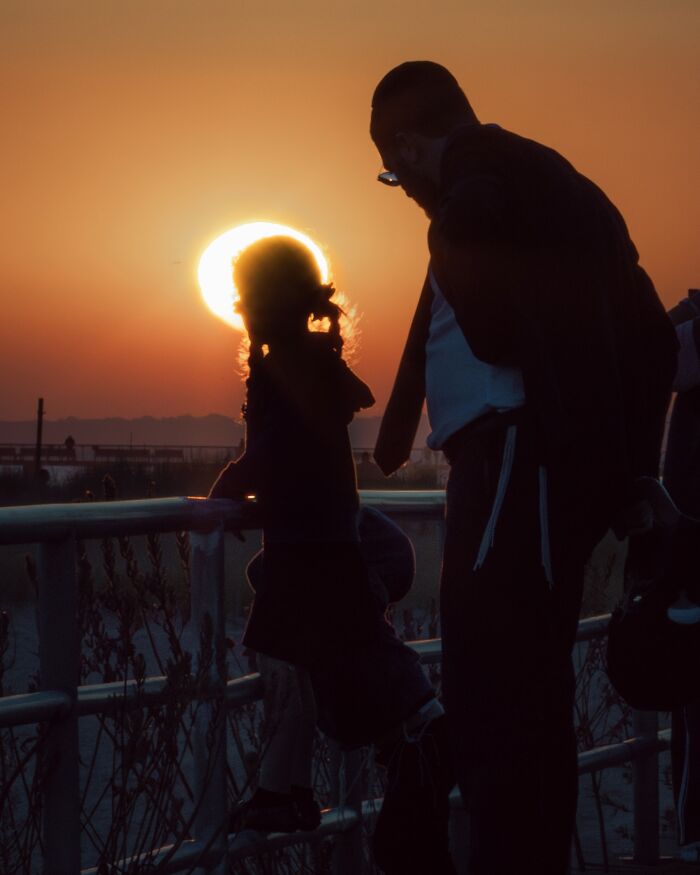 Silhouetted street photo of two people by railing at sunset with cinematic lighting for striking street photos.