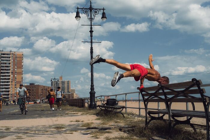 Man performing a parkour move over a bench on a vibrant urban street in a striking street photo that feels like a movie still