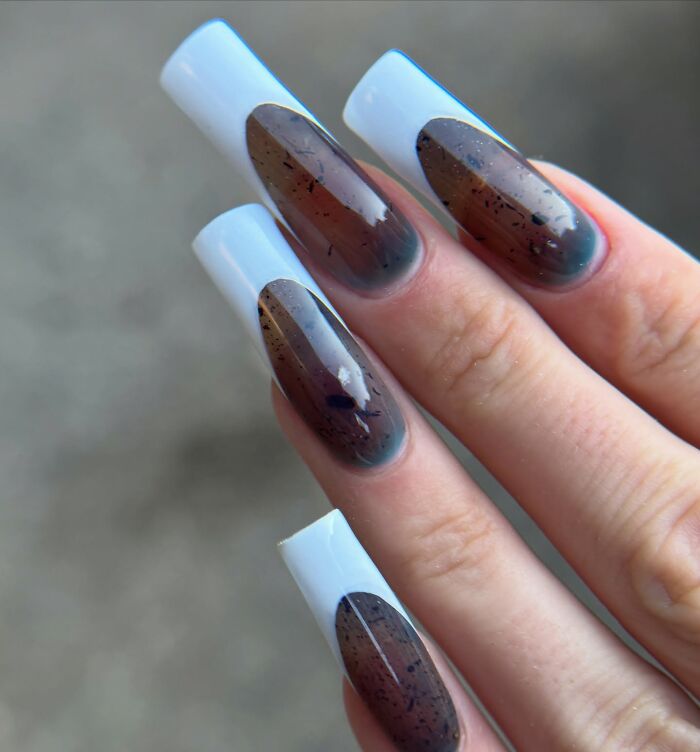 Long square nails with brown and translucent nail designs featuring black speckles and white tips, showing unique nail designs.