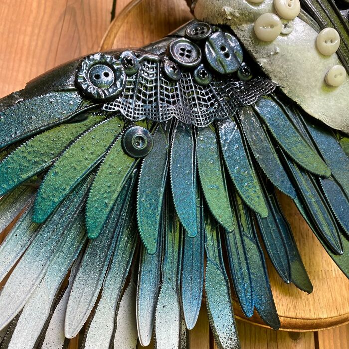 Intricate animal sculpture made from recycled trash materials resembling a bird with detailed wings mounted on wood.