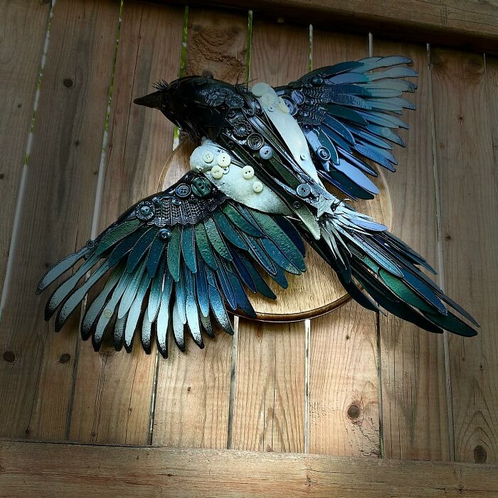 Intricate animal sculpture made from recycled trash materials resembling a bird with detailed wings mounted on wood.