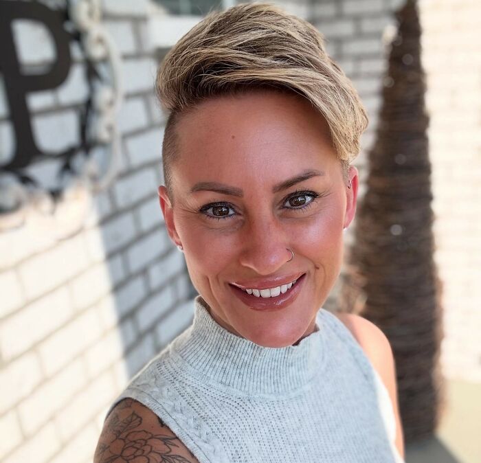 Smiling woman with a short hairstyle and tattoo, sharing experience about Charlie Kirk's favorite Starbucks drink and hidden message.