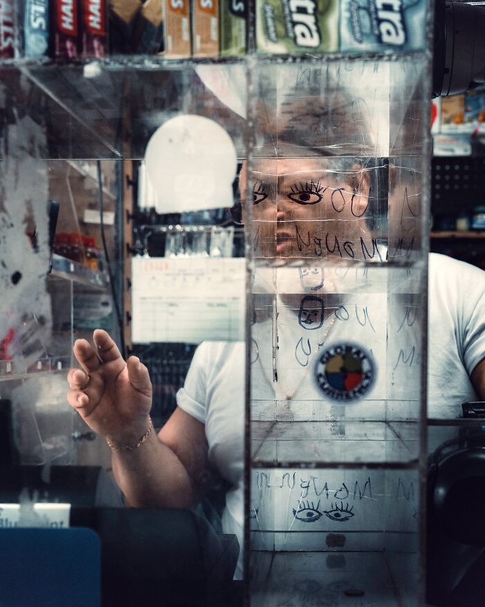 Man behind scratched glass with drawings and notes, creating a striking street photo with a cinematic feel.