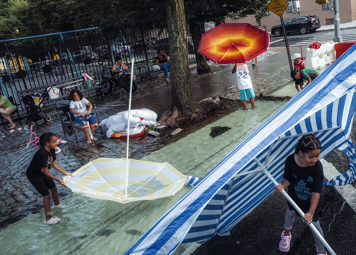 Children playing with colorful umbrellas and tents on a flooded urban street in a lively street photo scene.