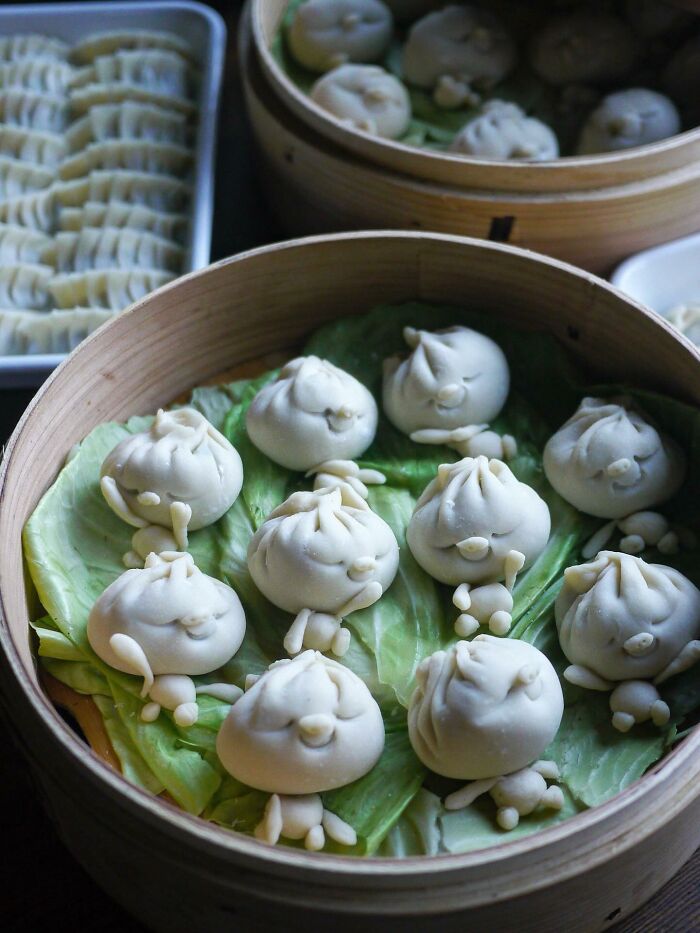 Steamed dumplings shaped like smiling faces on cabbage leaves in a bamboo steamer, creative meals for kids from Japan.