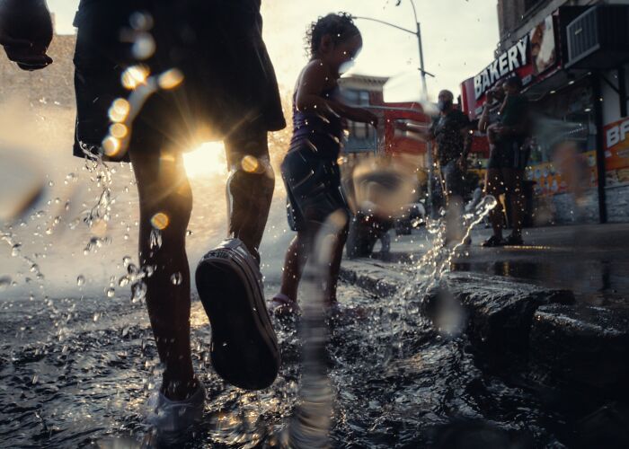 Child and adult splashing water on a city street at sunset in striking street photos that feel like movie stills.