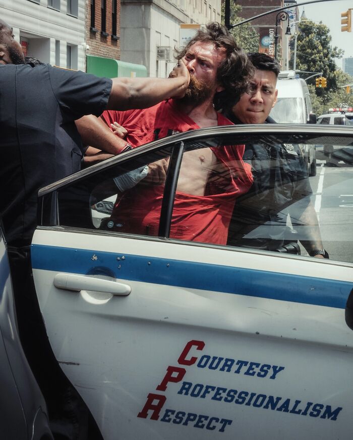 Street photo capturing a tense moment between police officers and a man near a patrol car, evoking cinematic drama.