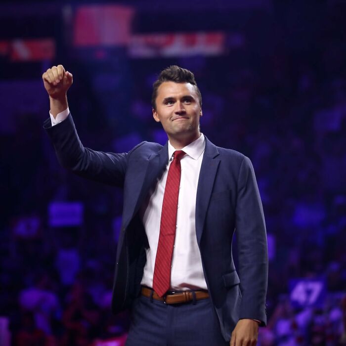 Charlie Kirk in a suit and red tie raising his fist on stage, linked to predicted passing in eerie post years ago.