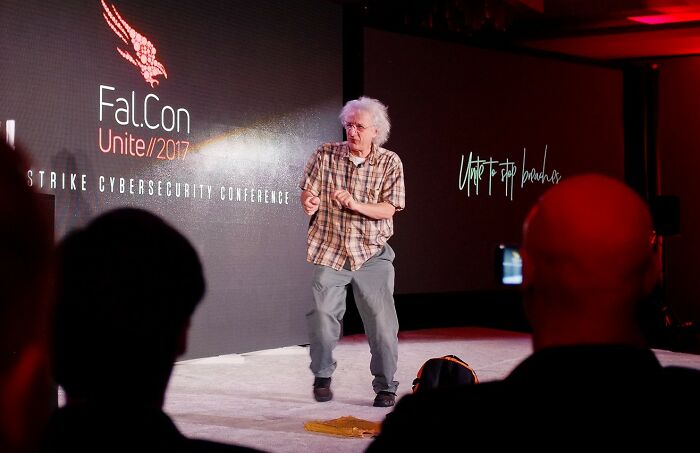 Speaker with white hair presenting at Fal.Con Unite 2017 cybersecurity conference, illustrating bold decisions with massive impact.