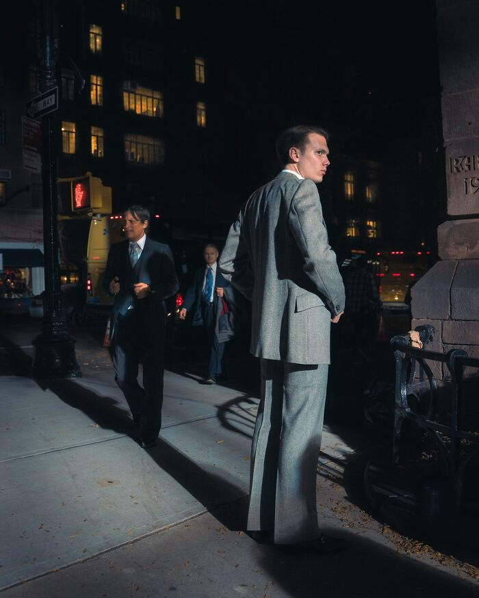 Young man in a gray suit standing on a dimly lit city street, capturing striking street photos with a cinematic feel.