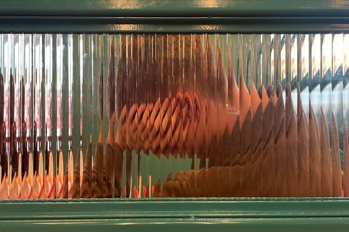 Distorted reflection of a person through ridged glass, showcasing a creative and funny street photo capturing life's humorous side.