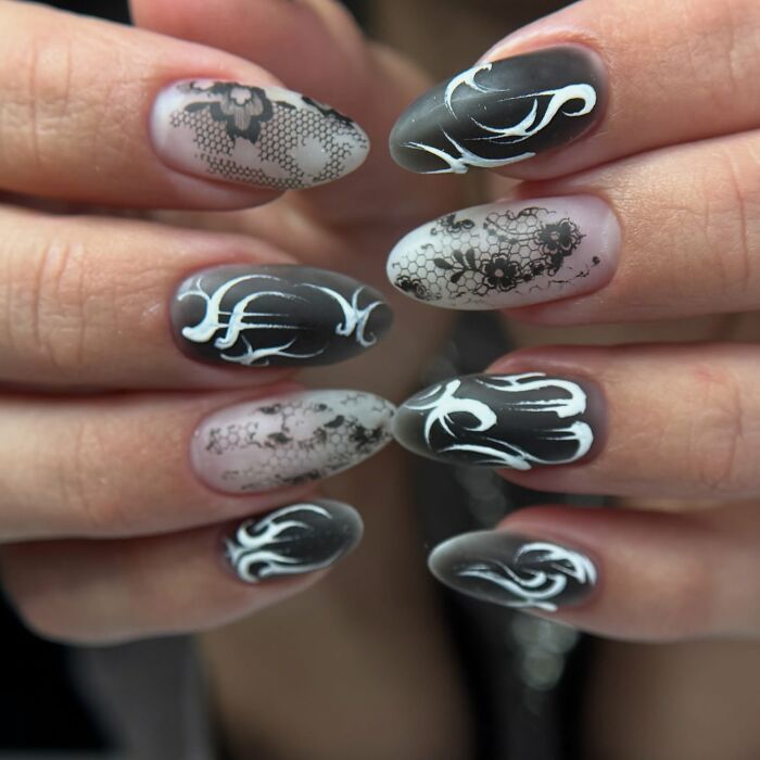 Black and white nail designs featuring intricate lace patterns and bold flame-like white accents on matte nails.