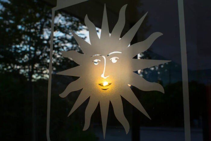 Sunlight creating a glowing face effect on a window decal, a serendipitous moment captured by street photographer in everyday life.