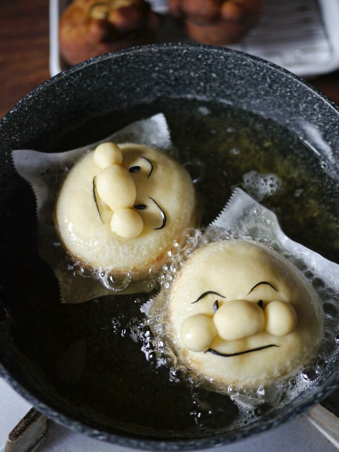 Creative meals for kids featuring six smiling, sugar-dusted bread rolls shaped like faces in a white tray.