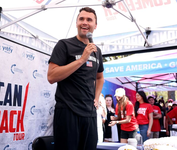 Man speaking at an event with crowd in background, capturing mass fury after Charlie Kirk&rsquo;s funeral compared to historic moments.