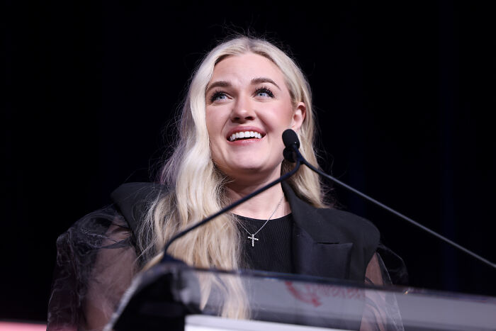 Erika Kirk speaking at a podium, smiling with long blonde hair, related to gesture during husband's funeral viral claim.