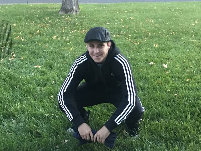 Young man crouching on grass, dressed in a black tracksuit and cap, related to Charlie Kirk suspect news.