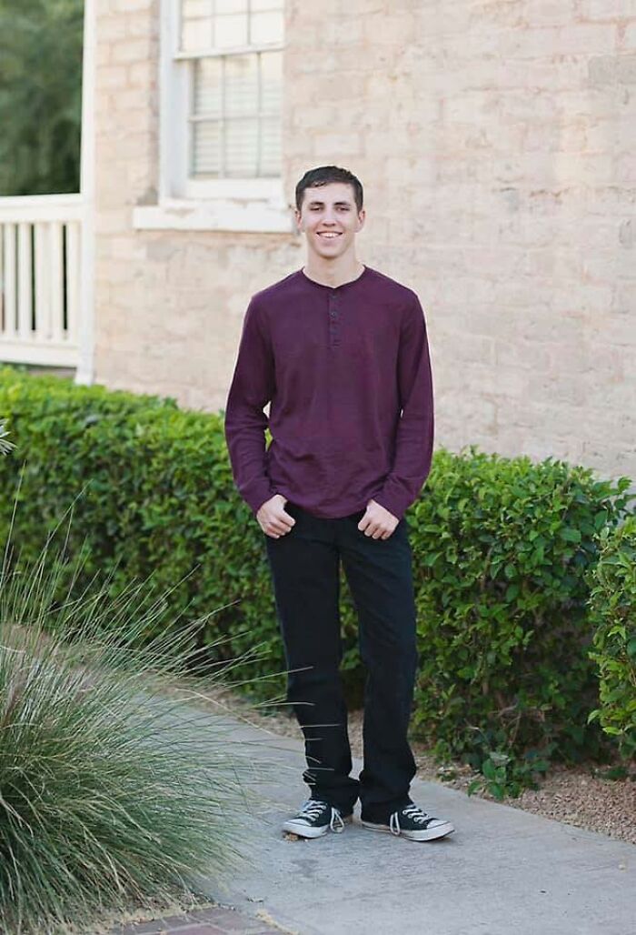 Smiling young man standing outside near bushes and a brick wall, representing shyest person suspect in police case.