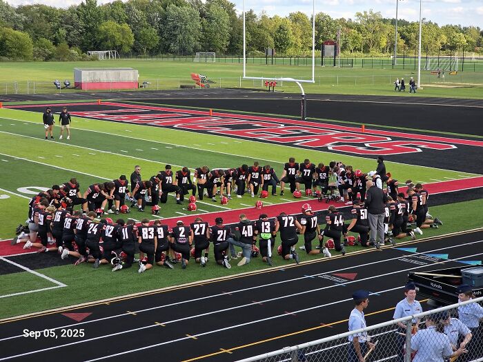 High school football team kneeling on field during practice after school takes strong and decisive action against player injury.