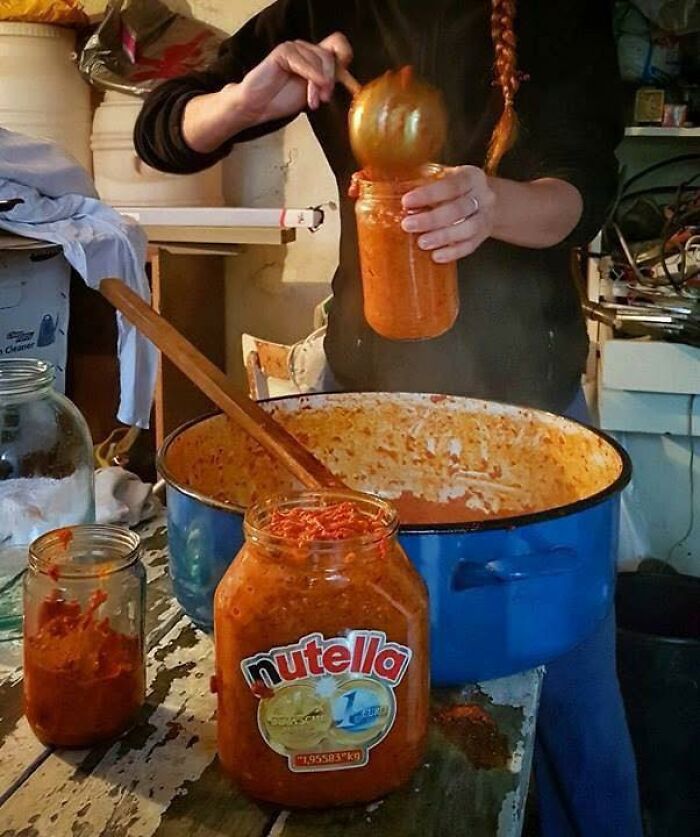 Person filling jars with homemade red pepper spread in a rustic kitchen, a scene only people raised in Eastern Europe get.