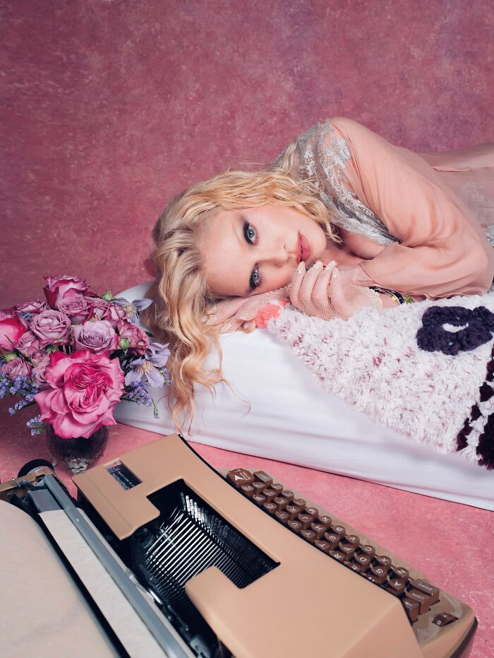 Madonna in a sheer lace dress lying on a bed with flowers and a vintage typewriter in a pink photo shoot setting Madonna in a sheer lace dress lying on a bed with flowers and a vintage typewriter in a pink photo shoot setting