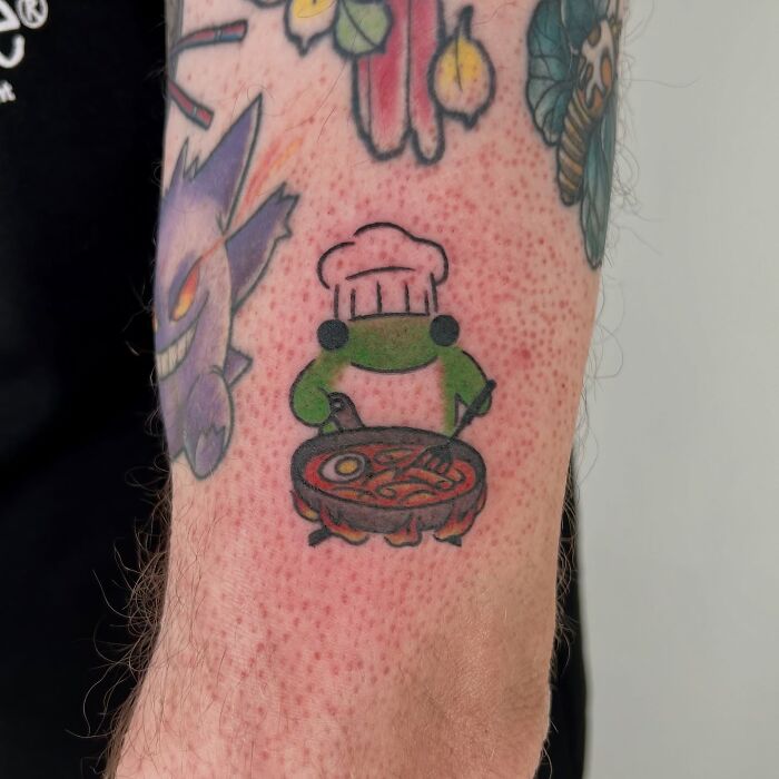 Small adorable frog tattoo wearing a chef hat and cooking, part of animal tattoos by Korean artist Buoy.