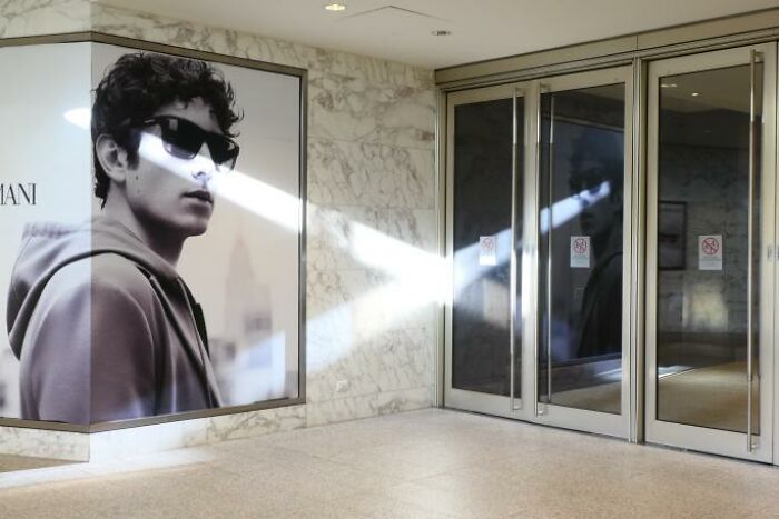 Black and white street photo showing light reflection creating a funny coincidence with a poster and glass doors.