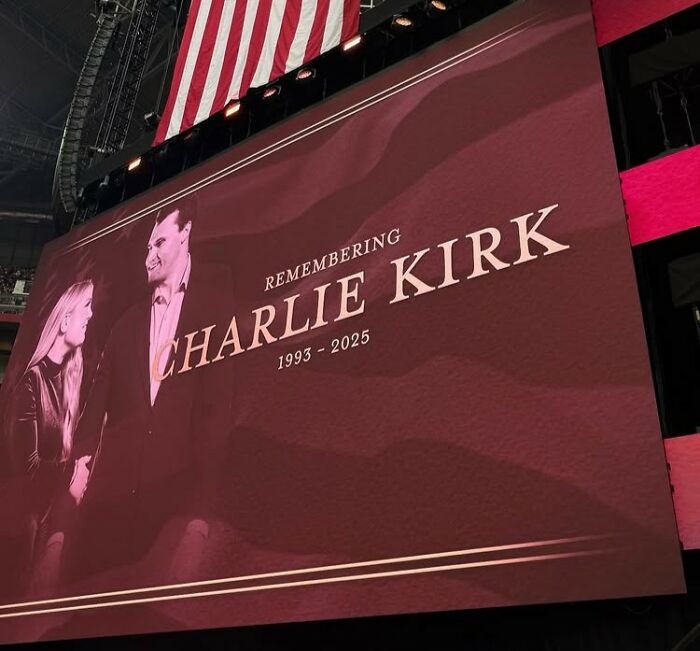 Memorial screen displaying remembering Charlie Kirk with dates 1993-2025 during a mass funeral event.