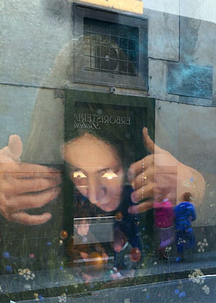 Reflection of a person’s face and hands blending with a street scene, capturing a funny coincidence in a street photo.