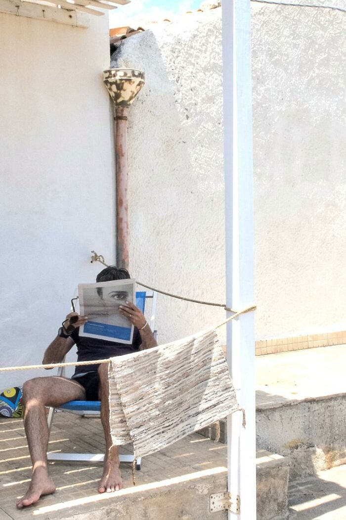 Man sitting on a chair reading newspaper with an eye on the paper aligning with his face in a funny street photo coincidence.