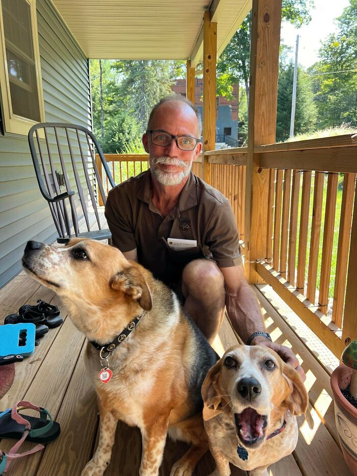UPS driver on porch with two adorable dogs, enjoying a friendly moment with pets during delivery.