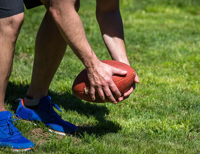 Man in blue sneakers holding football on grass, illustrating the lesson learned by woman who gave husband another chance