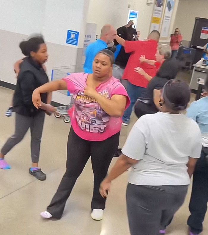 Angry mob inside Walmart confronting employee with tense gestures during chaotic scene in store aisles.