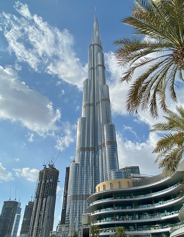 Burj Khalifa towering in Dubai skyline with palm trees and modern buildings under a partly cloudy sky. Burj Khalifa towering in Dubai skyline with palm trees and modern buildings under a partly cloudy sky.