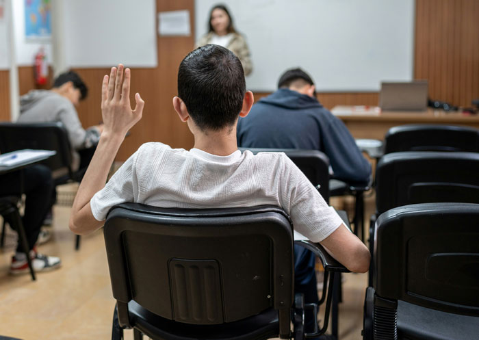 Student raising hand in classroom setting, highlighting focus on sleep as a real-life cheat code for problem solving.