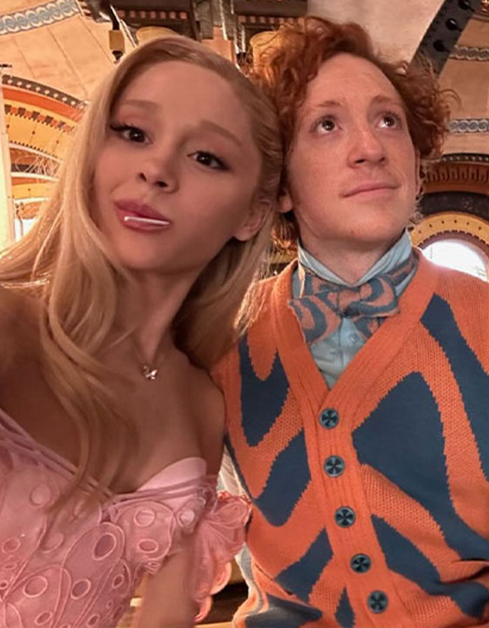 Ariana Grande's boyfriend Ethan Slater wearing a colorful sweater and bow tie posing indoors with Ariana Grande. Ariana Grande's boyfriend Ethan Slater wearing a colorful sweater and bow tie posing indoors with Ariana Grande.