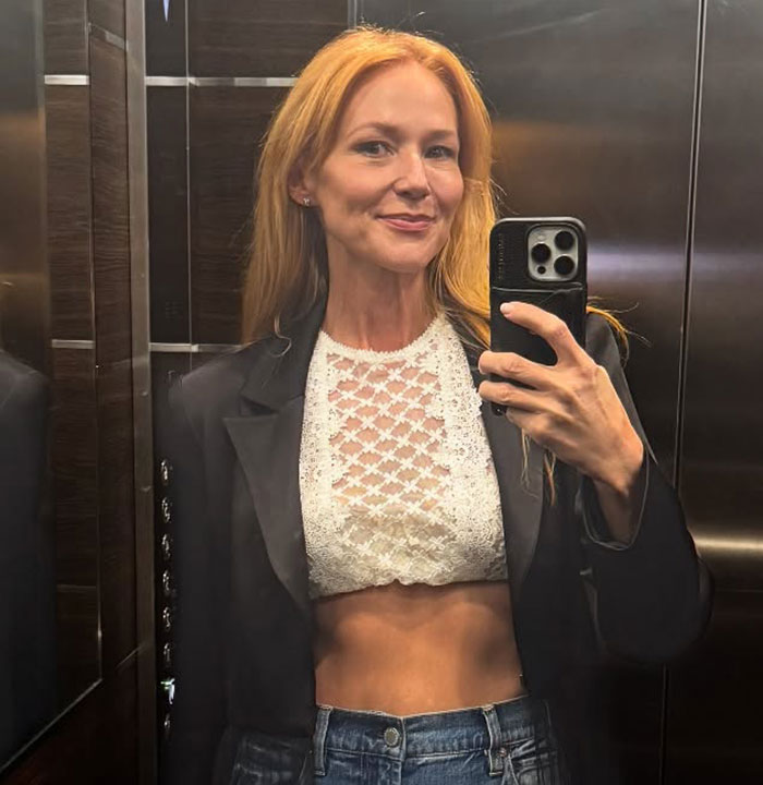 51-year-old 90s star showing off toned body in a white lace crop top and jeans, taking a mirror selfie in an elevator.