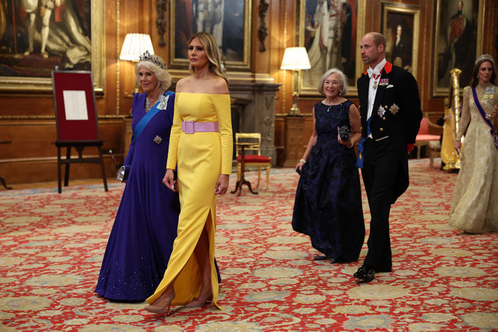 Melania Trump wearing a yellow optical illusion dress at a Windsor banquet with guests in formal attire walking behind her. Melania Trump wearing a yellow optical illusion dress at a Windsor banquet with guests in formal attire walking behind her.