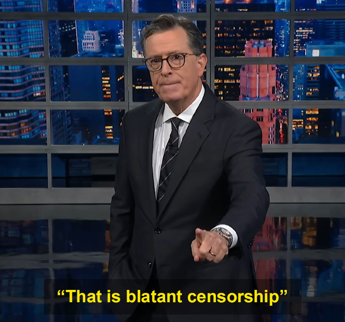 Stephen Colbert in a suit pointing, discussing censorship on a late-night talk show with cityscape studio background.