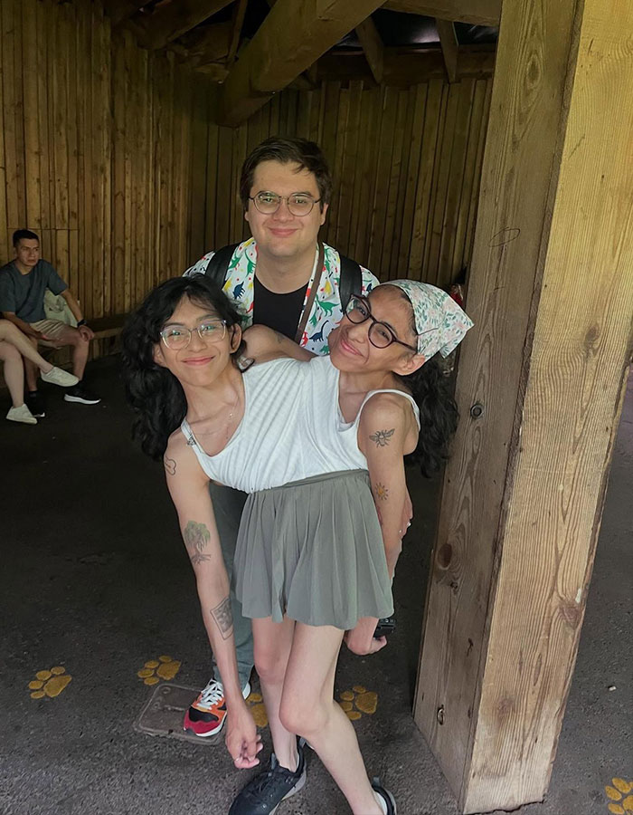 Conjoined twin Carmen Andrade smiling with her husband in a casual wooden setting, wearing glasses and casual attire.