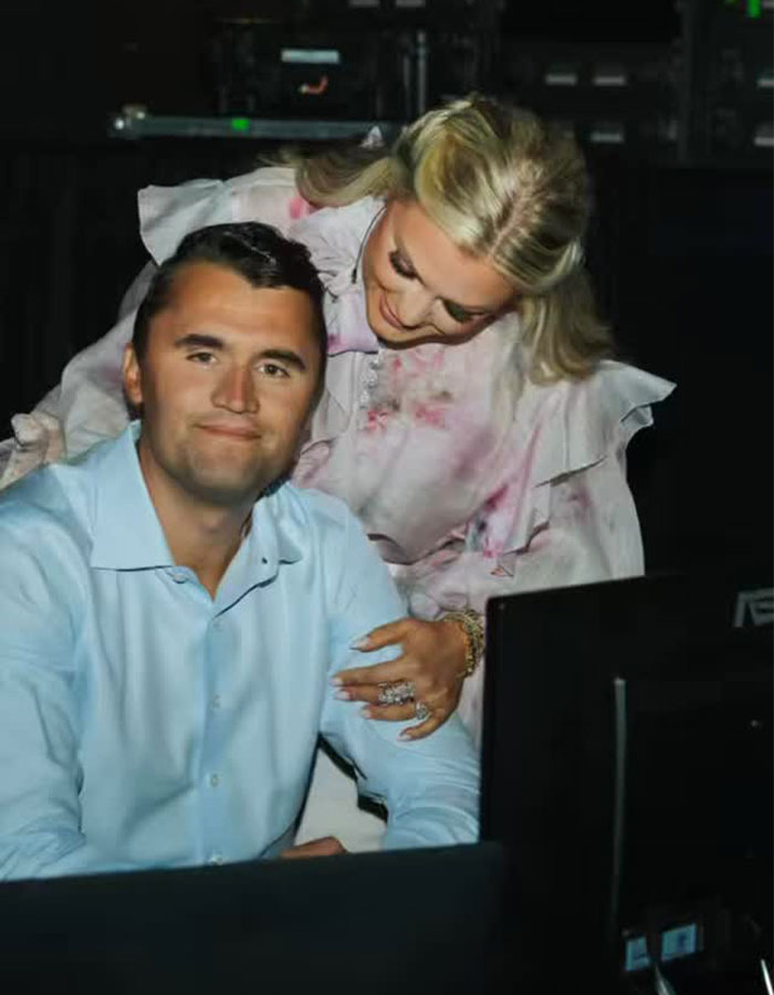 Erika Kirk speaking on justice for husband&rsquo;s assassin, showing support with a man in a dimly lit setting.