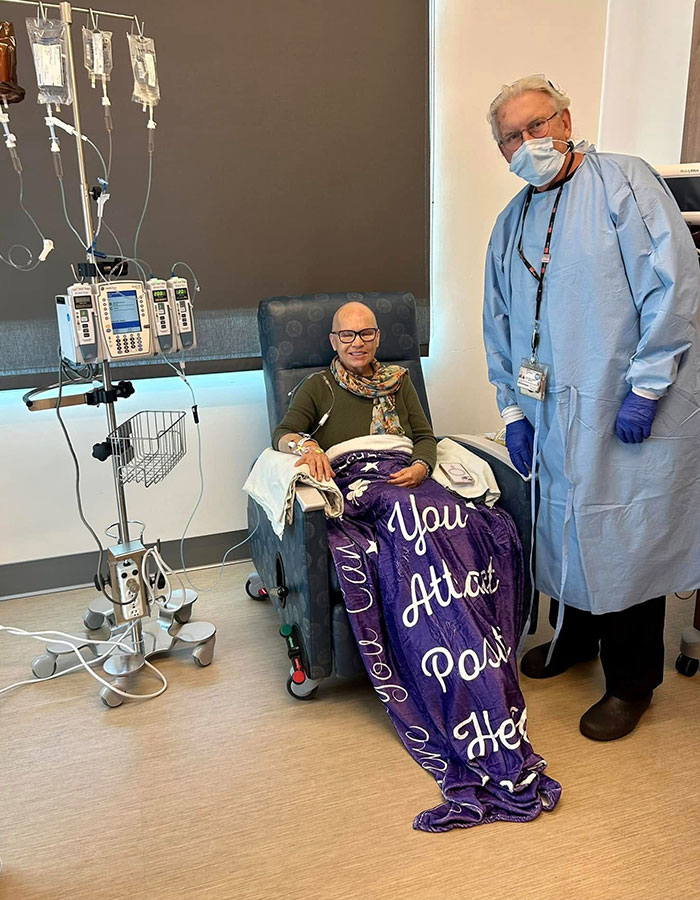 Woman receiving cancer treatment, sitting with an intravenous drip, accompanied by a masked healthcare professional.