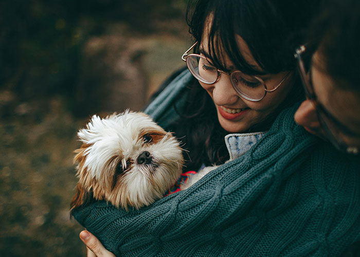Person holding and smiling at a small dog, illustrating common purchases people have ditched due to ridiculous price tags.